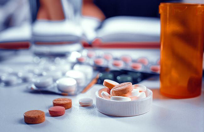 Orange and white tablets are laying on the table. Packs of the pills is in the bottle's cap. Blurred image of tablets packs on the background.