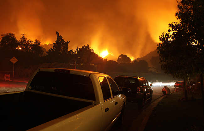 Residents of a neighborhood sit by and watch a fire threaten their homes.