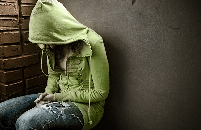 teenage girl siting against wall in a depressed state